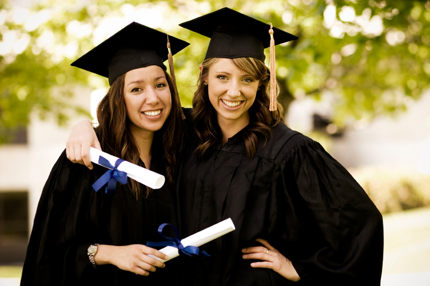 Two young women in cap and gown holding diplomas